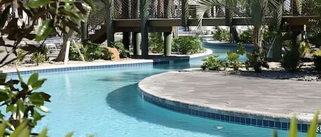 A swimming pool with a curved edge, surrounded by palm trees and other greenery.