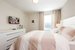A hotel room with a bed, a TV mounted on the wall, a dresser, and a window with curtains. - 6BR Villa w/ Pool & Game Room Near Disney (Davenport)
