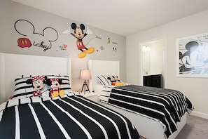 Een hotelkamer met twee bedden, elk voorzien van zwart-wit gestreept beddengoed, een muurdecoratie van Mickey Mouse en een spiegel.
