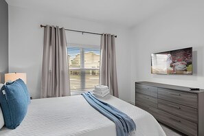 Ein Schlafzimmer mit Bett, Schminktisch, Fenster mit Vorhängen und einem Bild an der Wand.