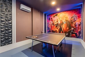 A ping pong table in a room with a geometric wall design and a vibrant poster featuring characters. - Luxury 7BR Villa w/ Pool & Game Room (Kissimmee)
