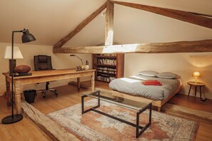 A loft bedroom with a sloped ceiling, a wooden desk, a bookshelf, a bed with pillows, and a small side table. - New Listing (Rouède)
