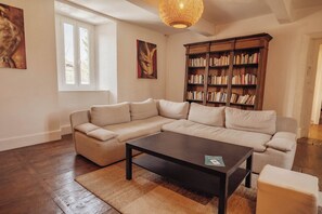 Ein Wohnzimmer mit einer Eckcouch, einem Couchtisch, einem Bücherregal und einem großen Fenster.