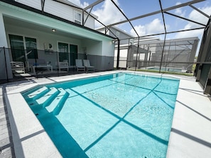 A swimming pool with a clear blue water, surrounded by a glass enclosure, and a patio area with chairs and a table. - Windsor Cay 5BR Villa w/ Pool & Game Room (Clermont)