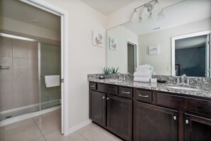 A modern bathroom with a glass shower enclosure, dark wooden cabinets, a granite countertop, and a large mirror. - Disney Escape, Family Retreat, Private Pool (Davenport)