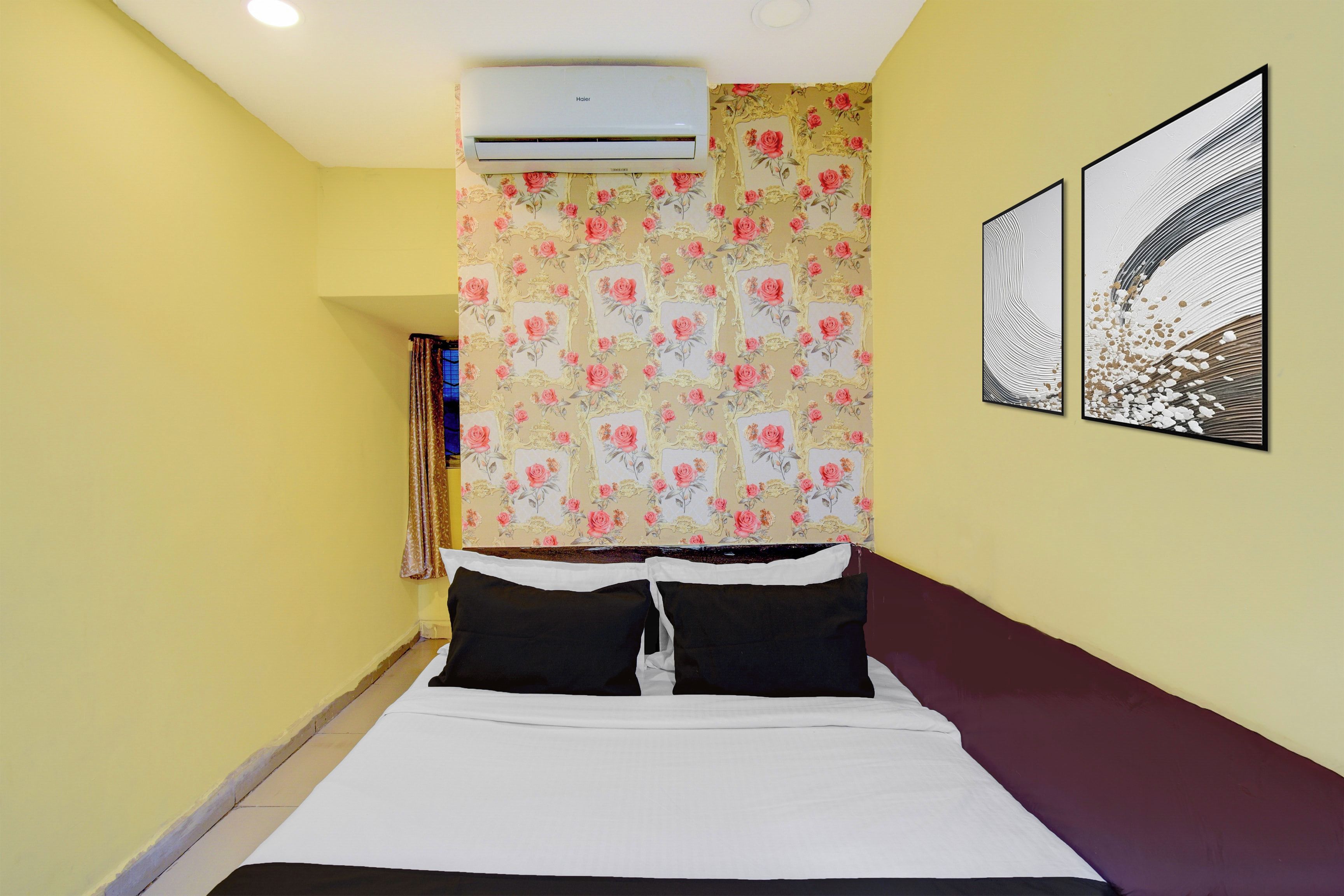 A hotel room with a bed, an air conditioner, floral wallpaper, and two framed artworks on the wall.