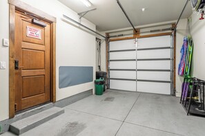 A garage with a wooden door, a closed garage door, a trash bin, and sports equipment hanging on the wall. - Private Hot Tub | On Golf Course (Mammoth Lakes)