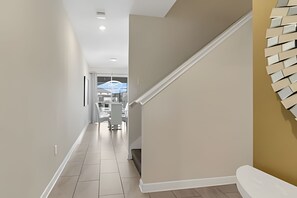 A modern interior with a staircase, a dining area in the background, and a wall-mounted light fixture. - 4BR Storey Lake Home, Sleeps 10 (Kissimmee)
