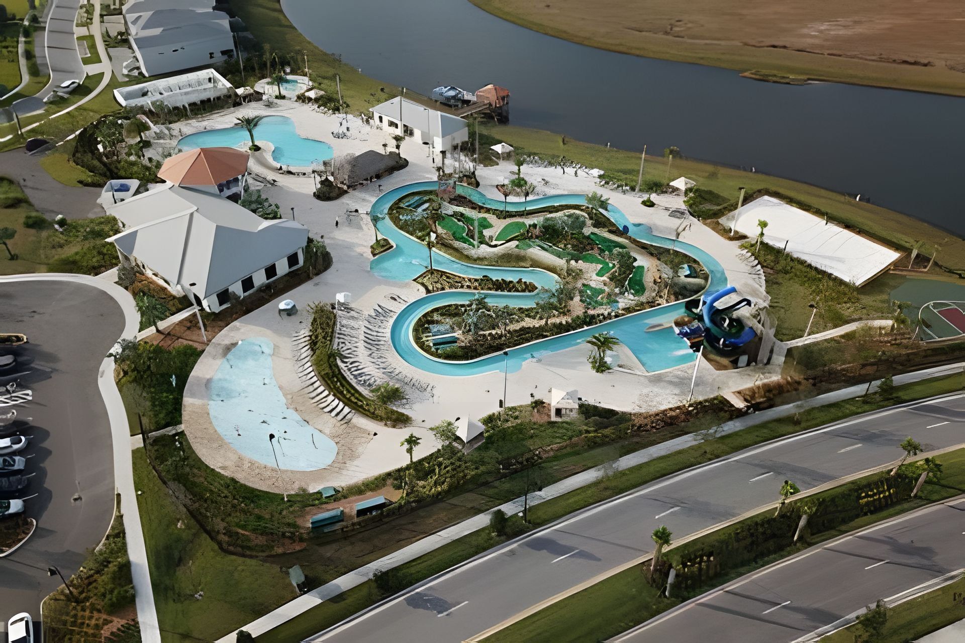 An aerial view of a resort with multiple swimming pools, a large central pool, and a parking area.