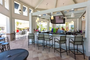 A spacious outdoor bar area with high ceilings and large windows, featuring multiple seating arrangements and a television screen. - 5BR Storey Lake Home, Sleeps 12 (Kissimmee)