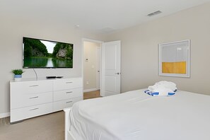 A hotel room with a bed, a TV mounted on the wall, a white dresser, a door, and a framed picture on the wall. - 5BR Storey Lake Home, Sleeps 12 (Kissimmee)