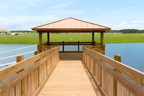 A wooden pier leading to a gazebo over a body of water, with a golf course in the background. - 5BR Storey Lake Home, Sleeps 12 (Kissimmee)