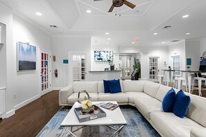 A modern living room with a white sectional sofa, a coffee table, and a TV mounted on the wall. - 3BR Lucaya Village Home Near Disney (Kissimmee)