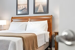 A neatly made bed with white linens and a wooden headboard, a bedside lamp, and two framed pictures on the wall. - 3BR Lucaya Village Home Near Disney (Kissimmee)