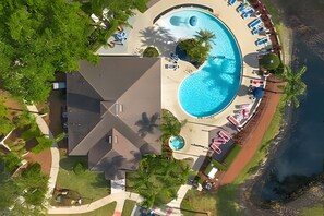 Eine Luftaufnahme eines Resorts mit einem großen Schwimmbad, Liegestühlen und einem Strandbereich.