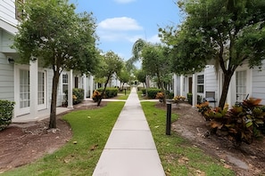 A pathway flanked by white buildings with large windows, leading to a central point. - 3BR Lucaya Village Home Near Disney (Kissimmee)