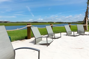 A row of beach chairs with a rope barrier, a sandy area, and a view of a body of water and distant buildings. - 4BR Storey Lake Home With Private Pool (Kissimmee)