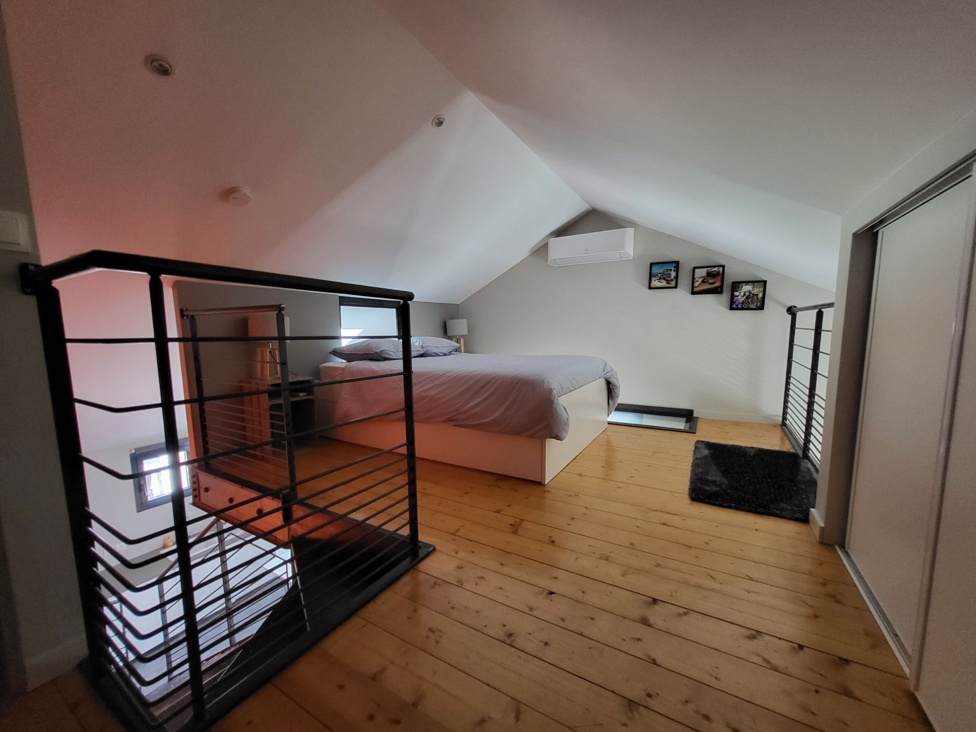 A bedroom with a sloped ceiling, a bed, a small desk, and a black metal railing.