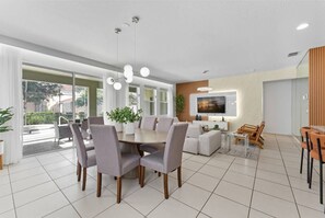 A spacious, well-lit room with a large dining table surrounded by chairs, a television mounted on the wall, and a large window providing natural light. - Solterra Resort 6br/5.5ba Pool/spa Up to 18 (Davenport)