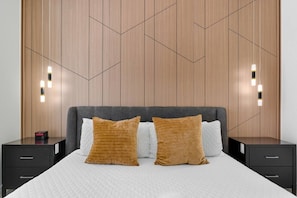 Ein modernes Schlafzimmer mit einem Kopfteil im geometrischen Muster, zwei Nachttischen mit Lampen und einem Bett mit zwei Kissen.