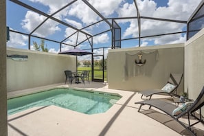 A covered outdoor swimming pool area with lounge chairs and a table, surrounded by a glass enclosure. - 5BR Home w/ Private Pool at Storey Lake (Kissimmee)