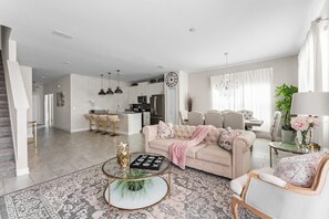 A spacious living room with a beige sofa, a coffee table, and a dining area with a chandelier. - 5BR Home w/ Private Pool at Storey Lake (Kissimmee)