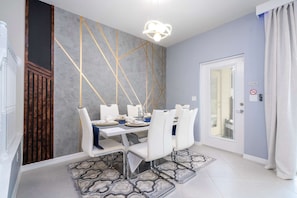 A dining area with a white table set for four, a modern chandelier, and a patterned rug. - 5BR Themed Villa w/ Private Pool (Clermont)