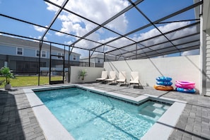 A swimming pool with a glass enclosure, surrounded by lounge chairs and inflatable rings. - 5BR Themed Villa w/ Private Pool (Clermont)