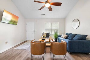 Una sala de estar con ventilador de techo, un sofá azul, dos sillones de cuero, una mesa de centro y un cuadro en la pared.