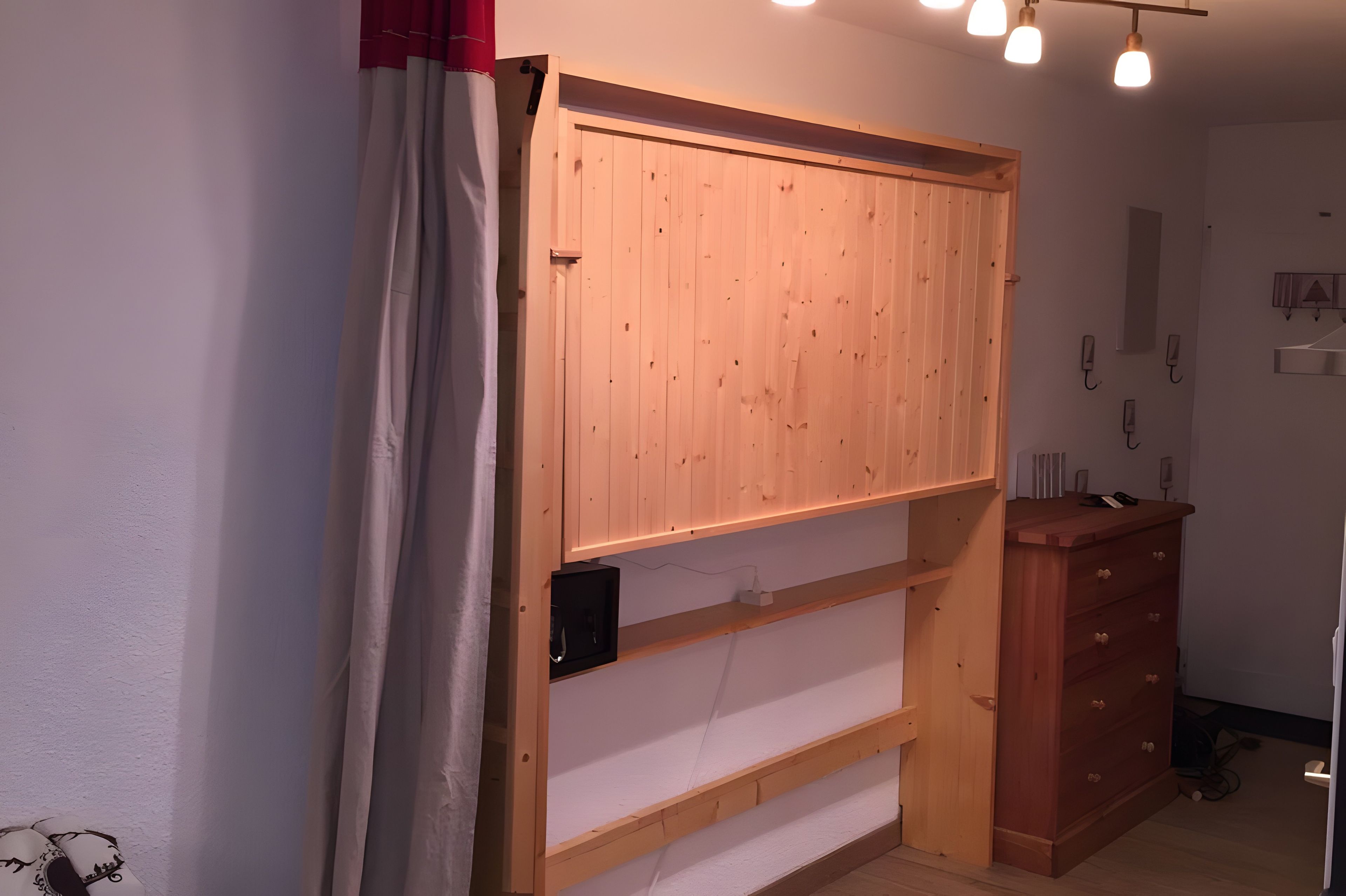 Ein Zimmer mit einem Holzschrank, einer weißen Wand und einem roten Vorhang.