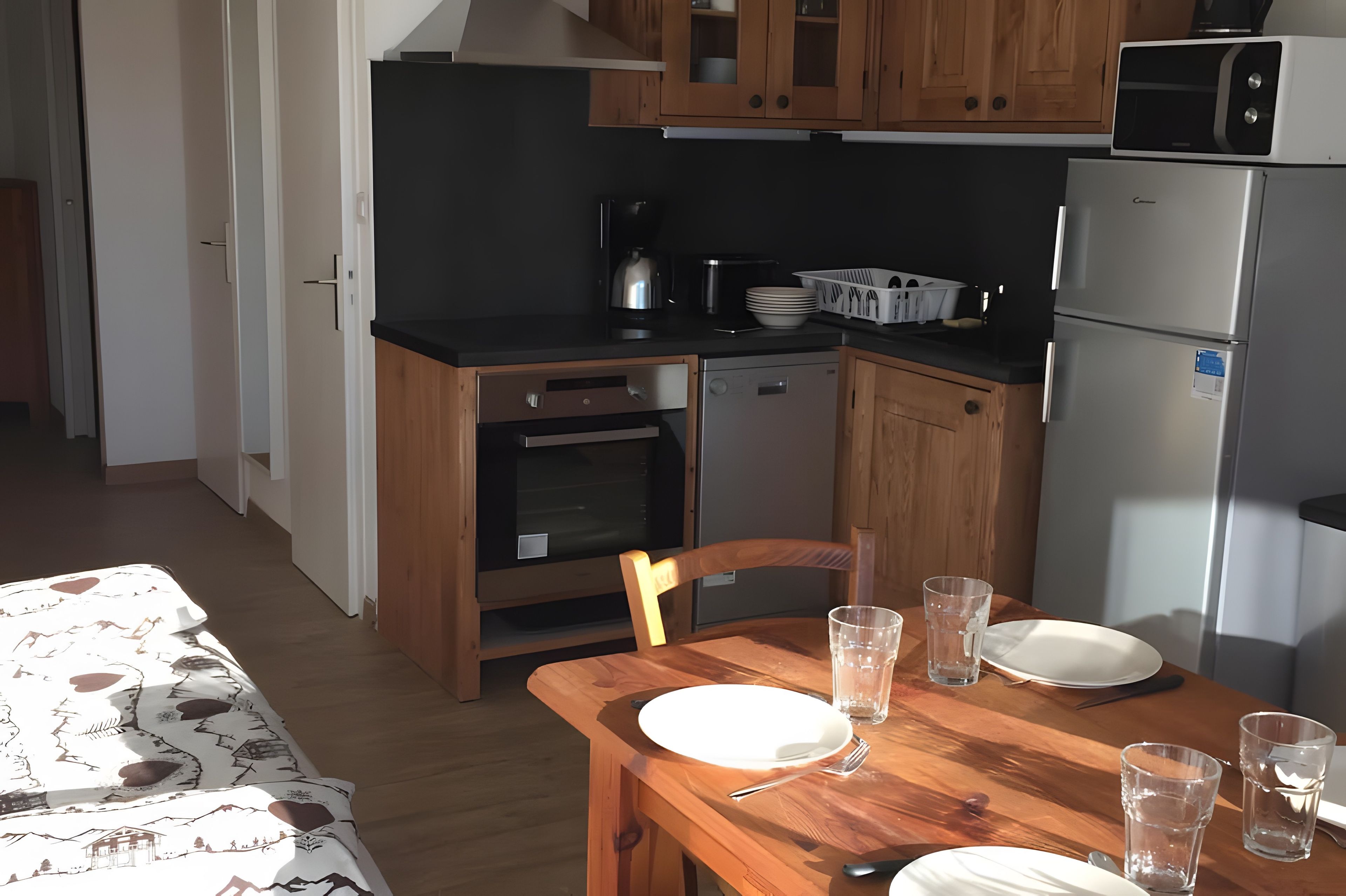 Ett kompakt kök med träskåp, en inbyggd ugn, en diskmaskin och ett kylskåp.