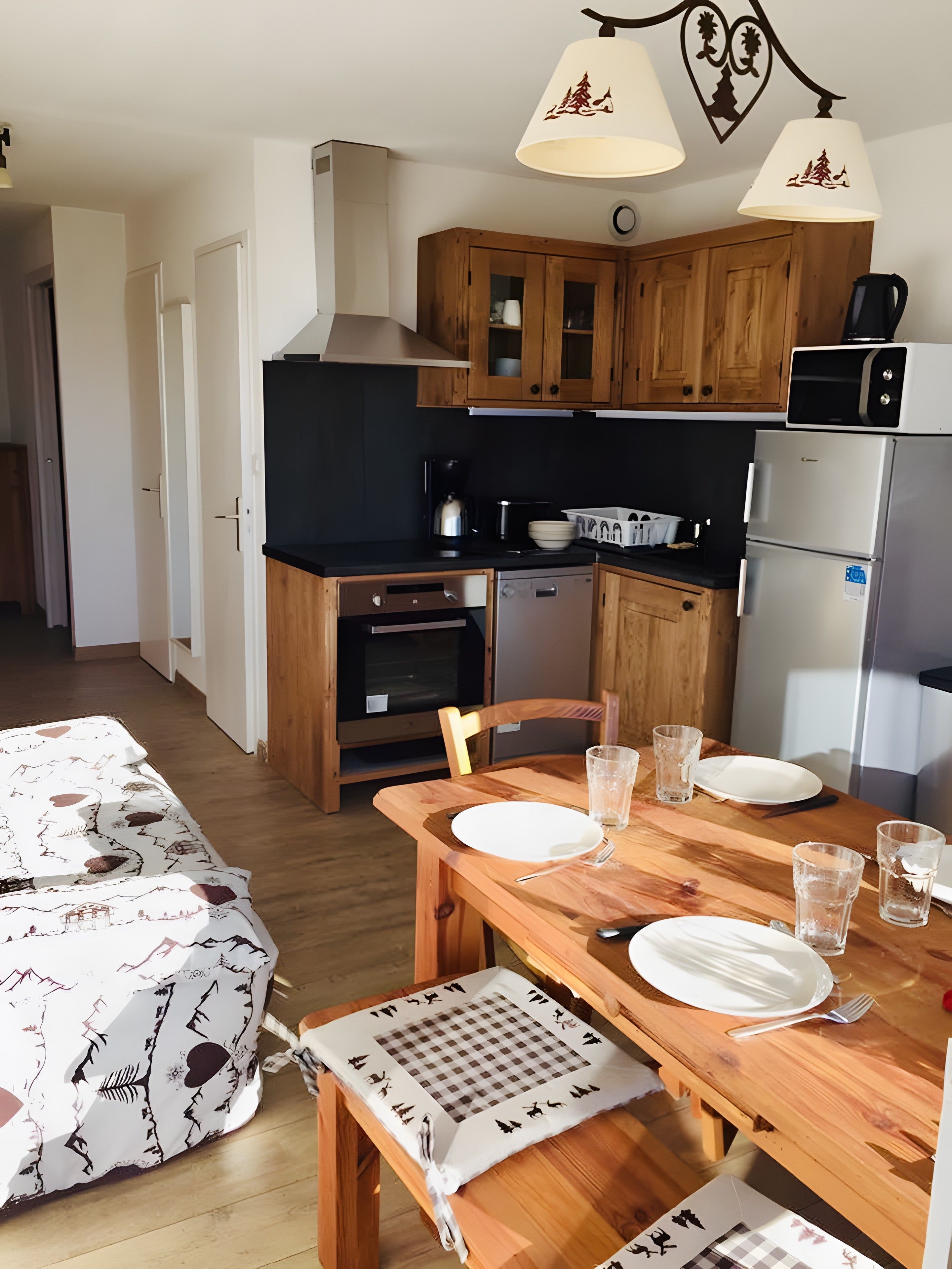 A compact kitchen with wooden cabinets, a refrigerator, a microwave, and a dining table set for two.