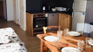A compact kitchen with wooden cabinets, a refrigerator, a microwave, and a dining table set for two.