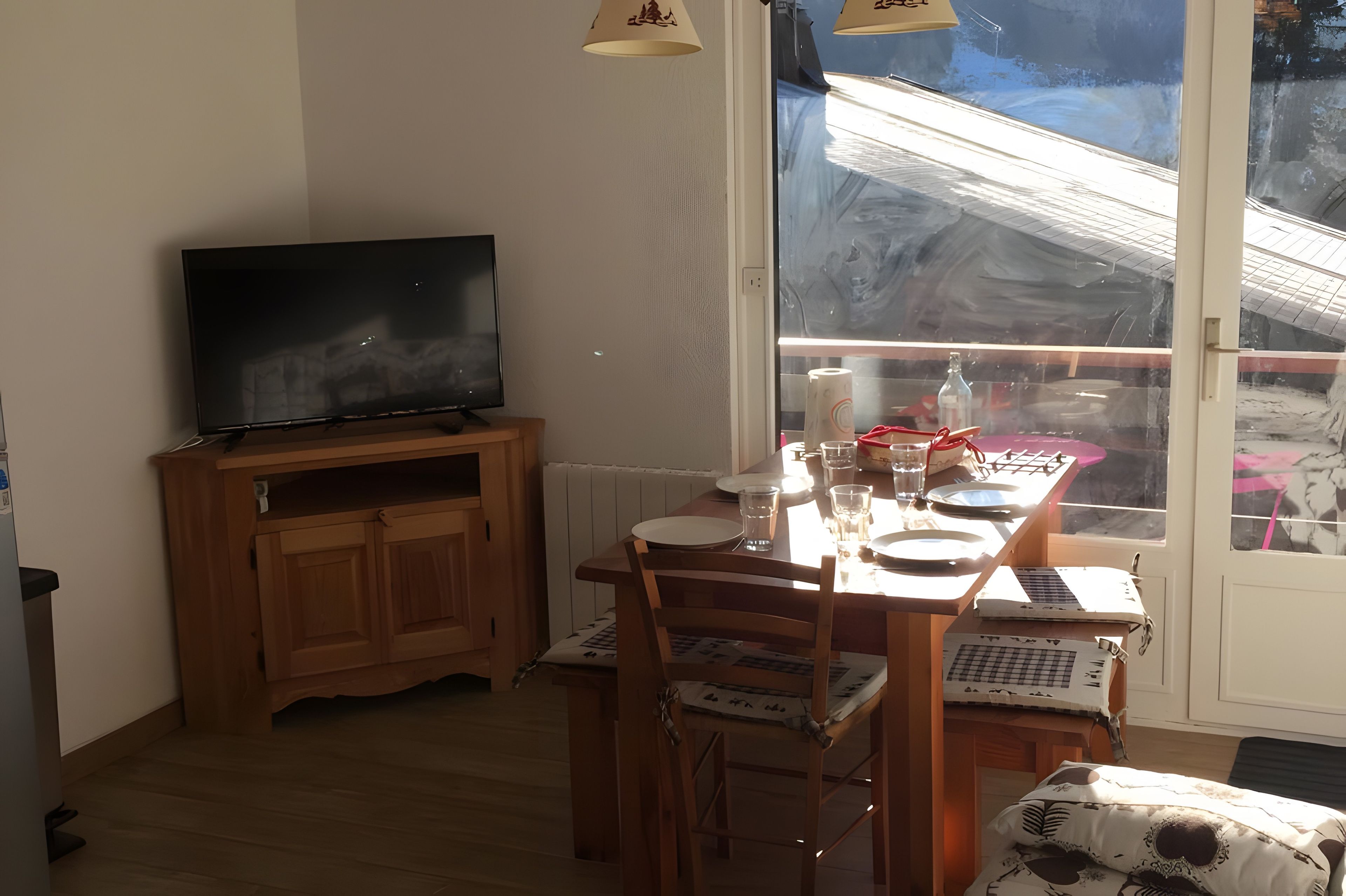 A room with a wooden cabinet, a television, a dining table with chairs, and a large window with a view of a construction site.