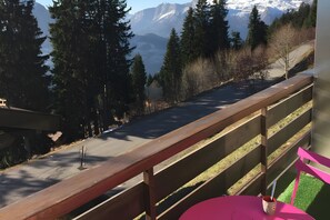 En vy över bergen från en balkong med ett träräcke, ett bord med en kopp på och en utsikt över en väg och träd.