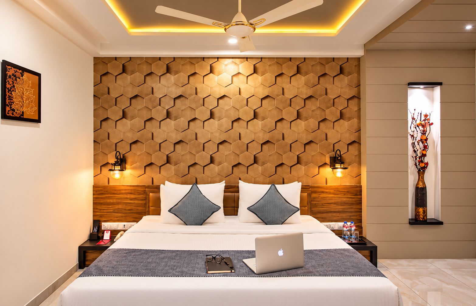 A modern hotel room with a large bed, a laptop, and a decorative vase.