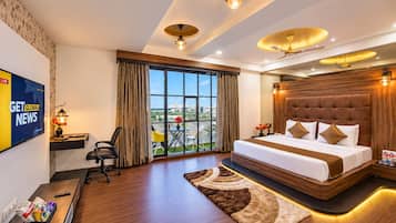 A modern hotel room with a large bed, a desk with a computer, a TV, and a view of the outdoors.