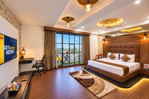 Habitación de hotel moderna con una cama grande, un escritorio con computadora, un televisor y vistas al exterior.