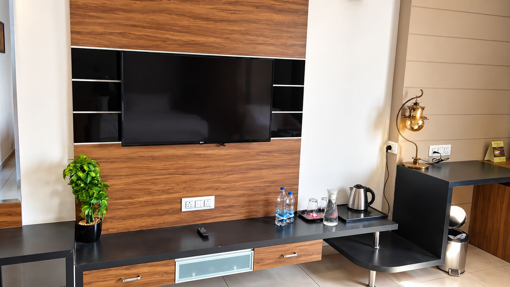 A modern kitchen with a built-in TV, a small plant, water bottles, a kettle, and a trash bin.