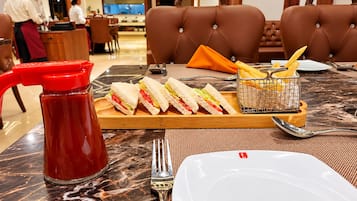 Ein Esstisch mit einer Sandwichetage, einer Saucenflasche, einem Korb mit Pommes und Besteck.