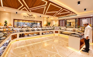 Buffet de Noventa Hotels & Resorts con un chef preparando comida, con un diseño moderno que presenta detalles de techo de madera y piso de mármol.