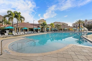 A swimming pool with lounge chairs and umbrellas, surrounded by palm trees and buildings. - Vista Cay 3BR Townhome- Near Universal (Orlando)