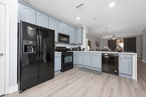 A modern kitchen with light blue cabinets, a black refrigerator, a microwave, an oven, and a dishwasher. - Vista Cay 3BR Townhome- Near Universal (Orlando)