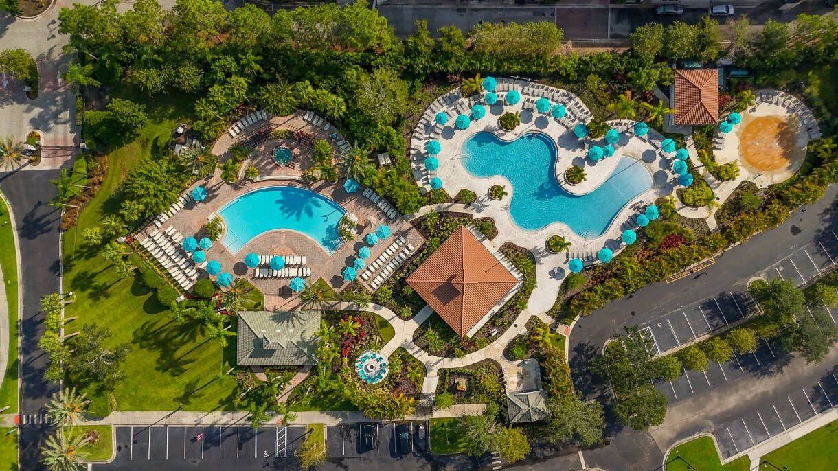 Eine Vogelperspektive eines Resorts mit mehreren Schwimmbecken, Liegestühlen und einem Parkplatz.