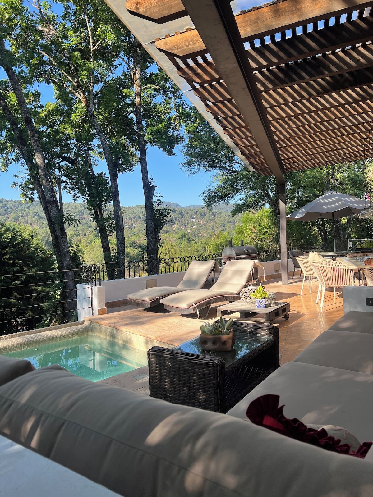 A poolside area with lounge chairs, a table with a plant, and a pergola overhead.