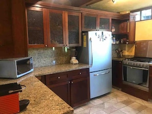 A kitchen with granite countertops, a stainless steel refrigerator, a microwave, a stove, and wooden cabinets. - Casa con alberca en Avandaro Valle de bravo (Valle de Bravo)
