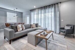 A modern living room with a grey sectional sofa, a wooden coffee table, and a grey armchair. - 5BR Windsor Island Home w/ Private Pool (Davenport)