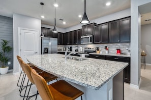 A modern kitchen with dark cabinets, a granite island, stainless steel appliances, and pendant lighting. - 5BR Windsor Island Home w/ Private Pool (Davenport)