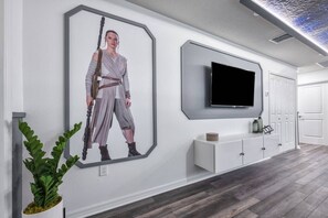 A modern hallway with a large framed artwork of a character, a flat-screen TV, and a minimalist console unit. - 5BR Windsor Island Home w/ Private Pool (Davenport)