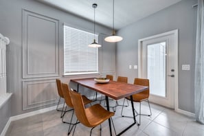 A dining area with a wooden table and six chairs, a bowl of fruit, pendant lights, and a window with blinds. - 5BR Windsor Island Home w/ Private Pool (Davenport)
